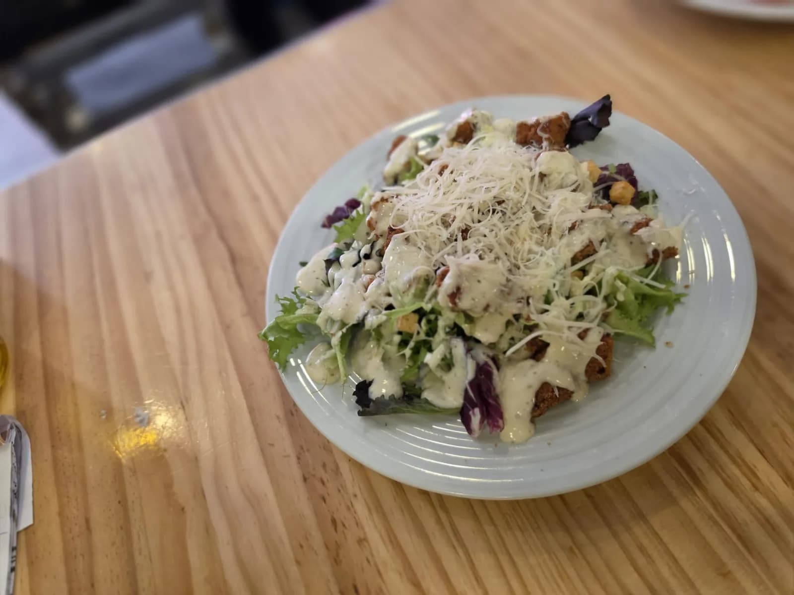 Ensalada César con pollo crujiente, parmesano rallado y salsa sobre mesa de madera
